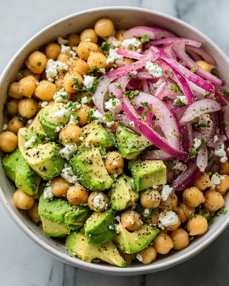 A close-up of a white bowl filled with a fresh salad showing three main layers: the bottom layer is light green sliced avocado with smooth texture, the middle layer has round, light brown chickpeas scattered all over, and the top layer consists of white crumbled feta cheese and thin purple onion slices mixed with small green parsley leaves; the salad is sprinkled with coarse black pepper and seasoning flakes, and a silver spoon is placed inside the bowl on the right side, all set on a white marbled surface photo taken with an iphone --ar 4:5 --v 7