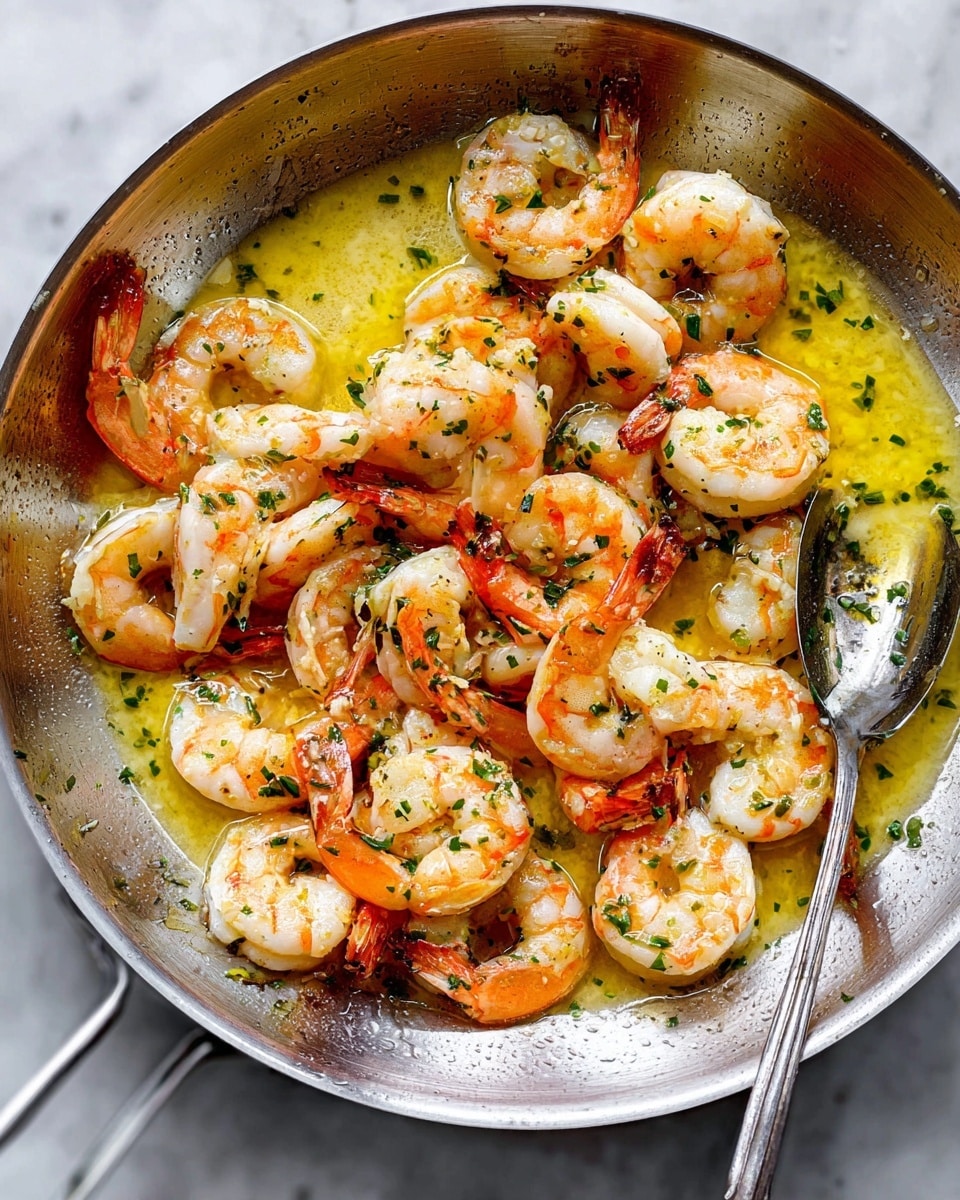 A white oval plate filled with a single layer of cooked shrimp that are pink and white, sitting in a golden buttery sauce with visible herbs and small bits of seasoning. On the top left of the shrimp, there are two torn pieces of soft white bread, lightly brushed with melted butter. At the bottom right, a lemon wedge adds a pop of yellow. A silver spoon rests in the shrimp, partially covered with a few shrimp and sauce. The plate is on a white marbled surface with small green herb pieces scattered around. photo taken with an iphone --ar 4:5 --v 7
