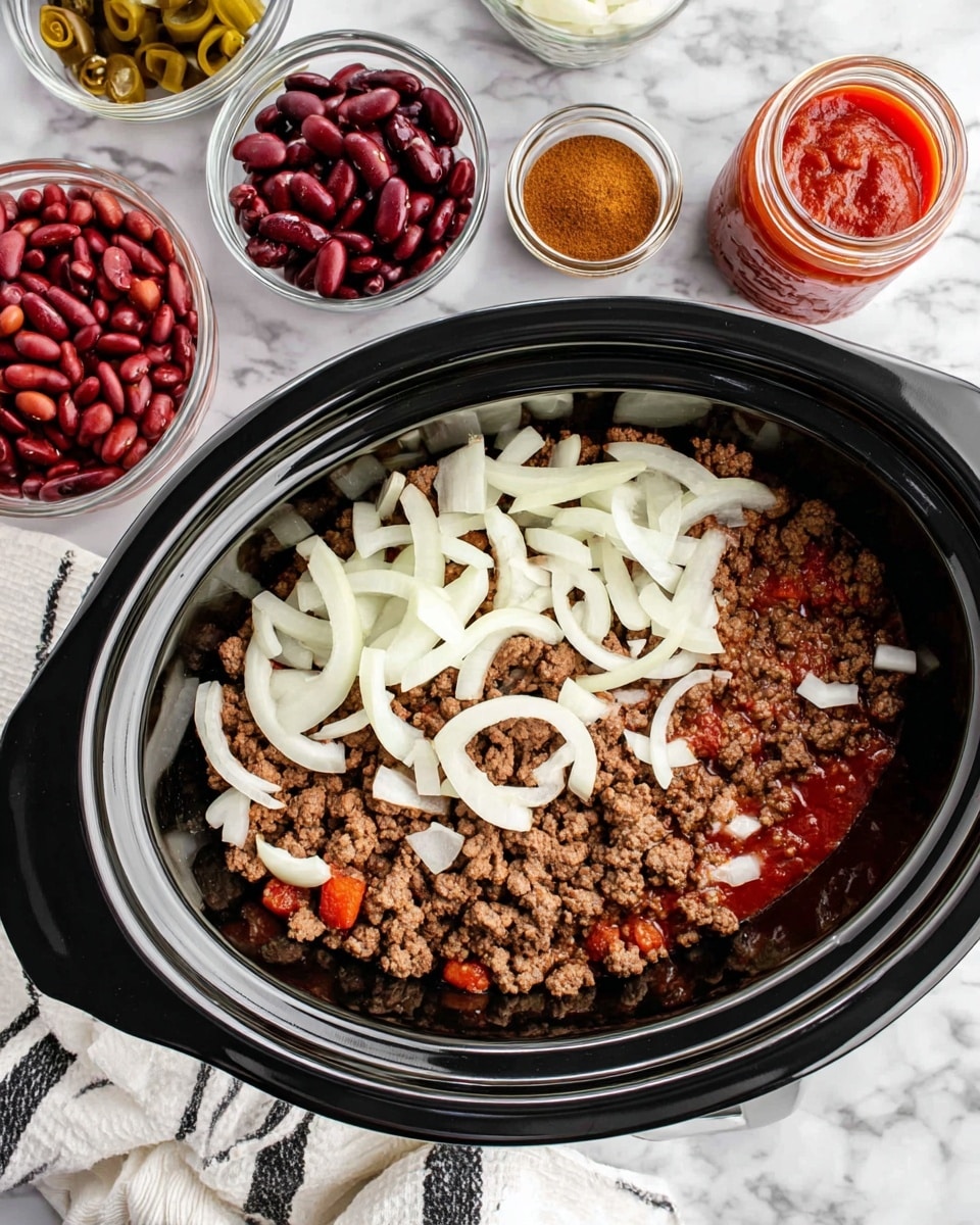 A black slow cooker holds two layers: the bottom layer is brown, crumbly cooked ground meat, and the top layer is raw sliced onions scattered unevenly on top. Surrounding the cooker are small clear bowls containing multicolored beans, dark red kidney beans, a bright red tomato sauce, a jar of thick red paste, and a bowl of light brown spices. The cooker sits on a white marbled surface with a white cloth with black stripes nearby. photo taken with an iphone --ar 4:5 --v 7