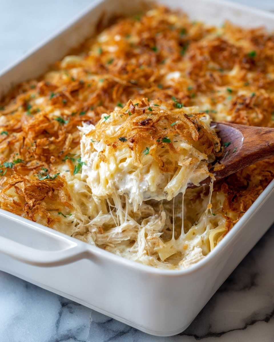 The dish is shown in a white oval baking dish filled with a baked pasta casserole. The bottom layer consists of light golden orzo pasta with a creamy texture, visible around the edges. The top layer is covered with melted cheese that is pale yellow with some light browning. On top of the cheese, there are thin, crispy fried onion rings that have a deep golden-brown color with darker browned edges. Scattered small pieces of fresh green herbs add a bright contrast to the warm colors of the casserole. The baking dish rests on a folded gray cloth on a white marbled surface. photo taken with an iphone --ar 4:5 --v 7