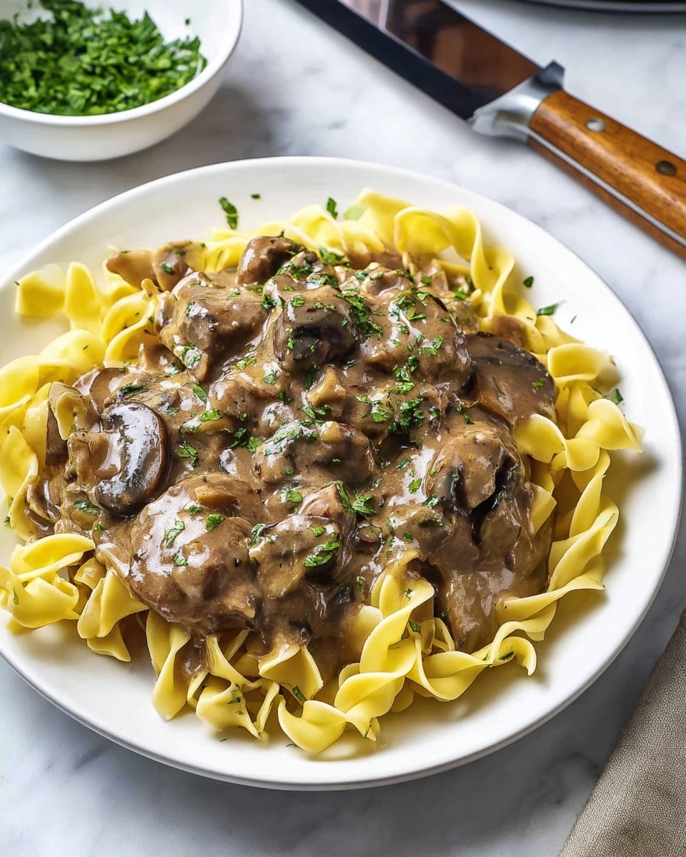 The image shows a close-up of a spoonful of creamy pasta with sliced mushrooms and small pieces of meat covered in a light brown sauce with green herbs, lifted above a white plate filled with the same creamy pasta dish. The pasta is curved and smooth, coated in sauce with visible bits of meat and mushroom, and garnished with small green herb pieces. The scene is set against a white marbled surface background. photo taken with an iphone --ar 4:5 --v 7