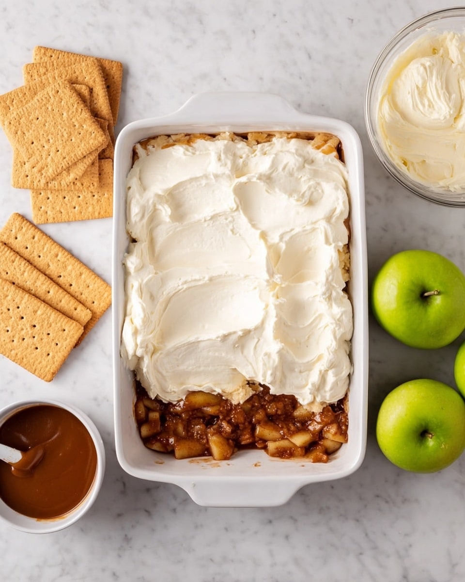A rectangular white dish shows a dessert in the making with two layers visible: the bottom layer is a chunky, brown apple mixture spread evenly, and on top, there is a thick white creamy layer being spread over the apples. On the left side near the dish, several rectangular light brown graham crackers are placed on a white marbled surface. Below them, a small white bowl holds a smooth dark caramel or dulce de leche sauce. To the right of the dish, two green apples and a bowl of extra apple filling sit on the white marbled background, along with a clear bowl containing the same creamy white mixture. photo taken with an iphone --ar 4:5 --v 7