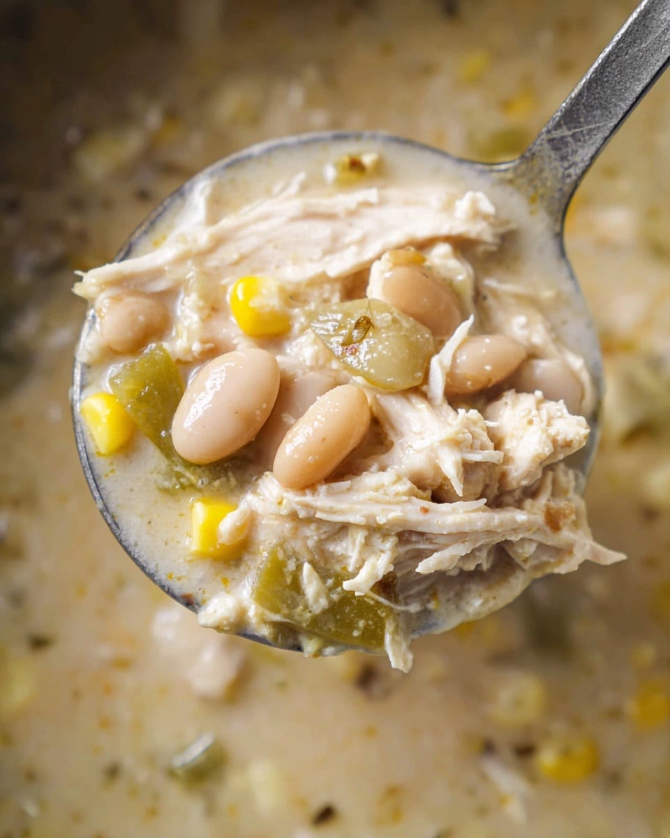 A close-up view of a metal spoon holding a thick soup filled with shredded white chicken pieces, light beige beans, pale yellow corn kernels, and small green vegetable bits, all mixed in a creamy light beige broth that looks smooth and slightly chunky. The background is a white marbled texture with more of the same soup visible. The spoon is filled with a dense mix of ingredients showing different textures, from soft shredded chicken to plump beans and corn, with hints of light seasoning sprinkled over the top photo taken with an iphone --ar 4:5 --v 7