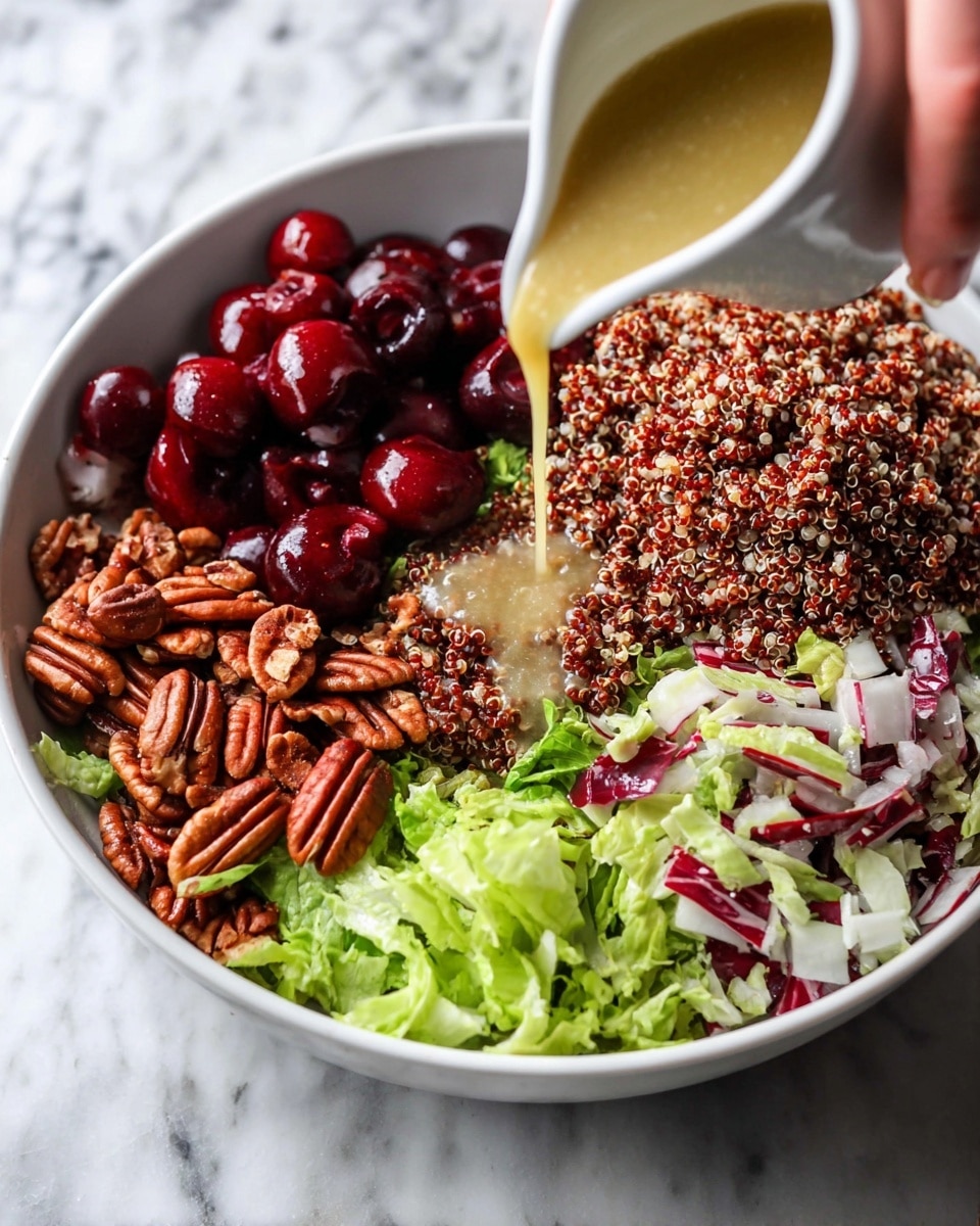 A white bowl on a white marbled surface holds a colorful salad arranged in five clear sections: dark red halved cherries on the left, bright shiny pecan nuts below them, deep red and white chopped radicchio on the bottom right, light green shredded lettuce on the top right, and a large pile of reddish-brown cooked quinoa at the top. A woman's hand pours light golden dressing from a small white pitcher onto the quinoa in the center of the bowl. The textures range from smooth and juicy cherries to crunchy pecans, leafy greens, and fluffy quinoa. Photo taken with an iphone --ar 4:5 --v 7