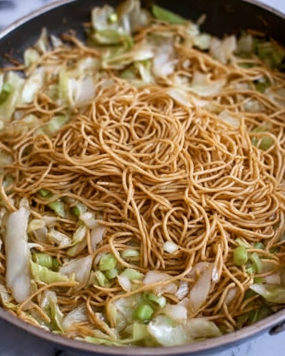 A close-up view of a frying pan filled with thin, light brown noodles mixed with pieces of white and light green cabbage and small bits of green onion scattered around. The noodles are cooked and slightly shiny, lying in a loose mound in the center. The cabbage pieces are scattered evenly around the noodles, with some cooked edges visible. The background is a white marbled texture. Photo taken with an iphone --ar 4:5 --v 7
