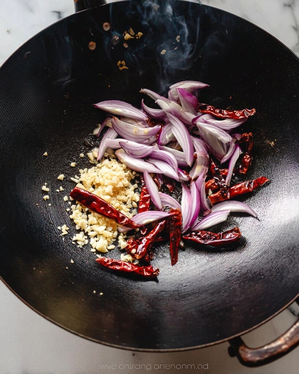 A large black wok holds several ingredients in layers: at the bottom, small minced pale yellow garlic pieces; on top of the garlic, uneven slices of purple and white onion arranged in a loose circle; resting on the onions are several whole dried red chili peppers scattered around. Light smoke rises slightly from the wok edges. The wok sits on a white marbled surface. photo taken with an iphone --ar 4:5 --v 7