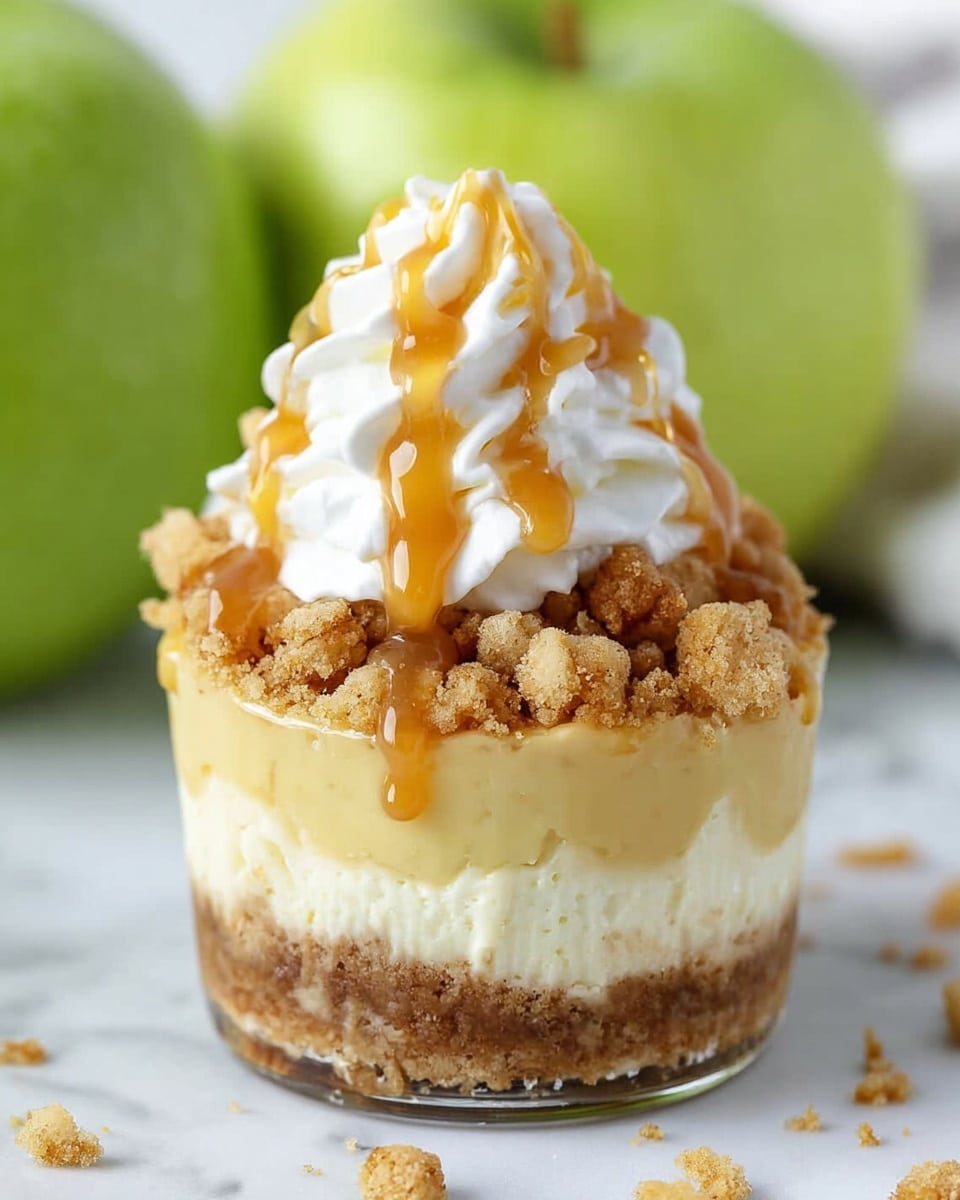 The image shows a close-up of a small dessert with four clear layers. The bottom layer is dense and crumbly, light brown with a rough texture. Above it is a thick, smooth pale yellow layer that looks creamy. On top of that is a crumbly light brown layer with small chunks, giving a crunchy look. The dessert is finished with a soft, white whipped topping drizzled with golden caramel sauce. It sits on a white marbled surface with blurred green apples in the background. Photo taken with an iphone --ar 4:5 --v 7