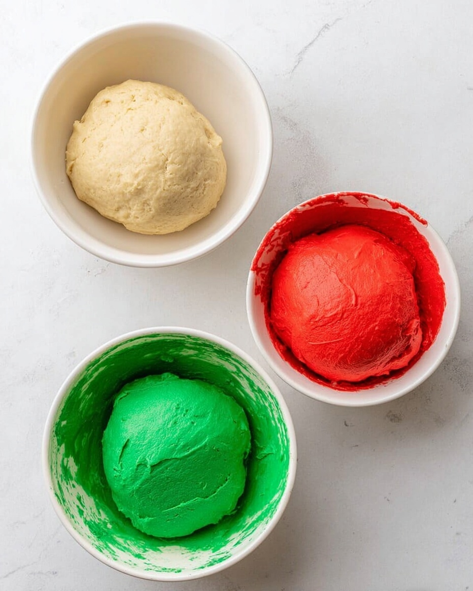 The image shows three white bowls placed on a white marbled surface, each holding a smooth ball of dough. The top bowl contains light beige dough with a soft, slightly textured surface. The bottom left bowl has bright green dough with a smooth and even texture, some green dough residue is visible on the bowl's sides. The bottom right bowl holds bright red dough, also smooth but with red streaks left behind inside the bowl. The colors are vivid and distinct, making each dough ball stand out clearly. photo taken with an iphone --ar 4:5 --v 7