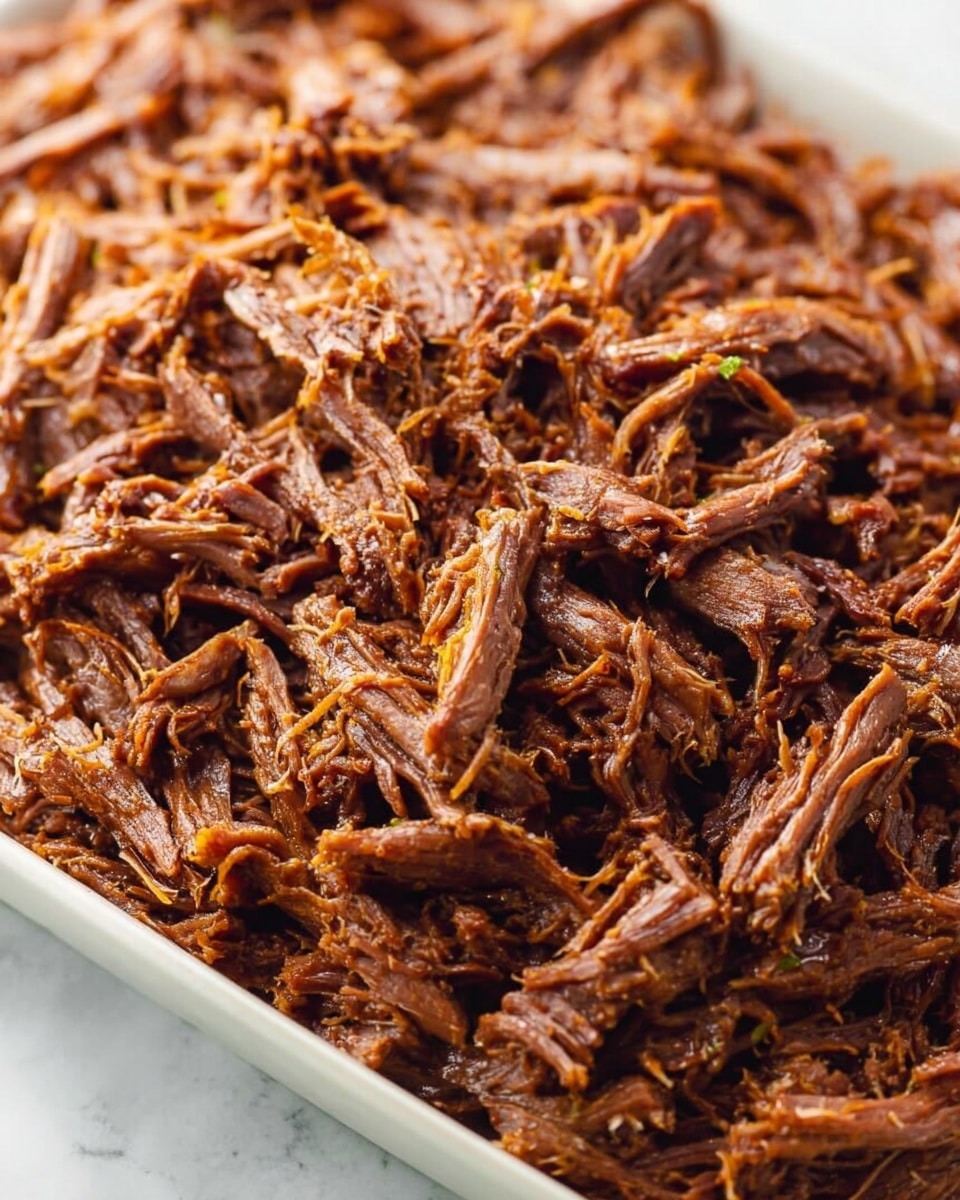 A close-up image showing a large pile of shredded, cooked meat with a rich brown color and fibrous texture, spread evenly in a white tray. The meat strands vary in size, with some thicker chunks and many thin, stringy pieces interwoven, creating a textured surface. The white tray contrasts with the dark brown meat, and the background is a white marbled texture. photo taken with an iphone --ar 4:5 --v 7