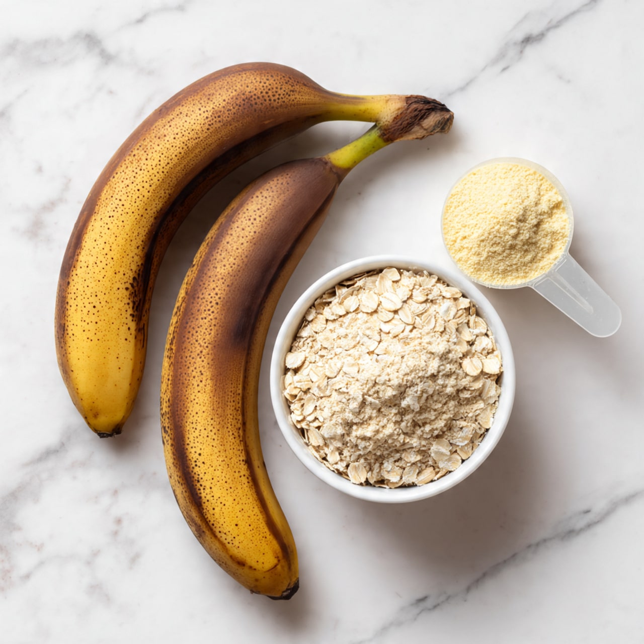 Two ripe bananas with dark brown skin lie side by side on a white marbled surface, with the stems pointing to the right. To the right of the bananas, there is a clear plastic scoop filled with light yellow protein powder. Below these items, a white bowl filled with light beige rolled oats sits on the white marbled surface. The image is bright and clear, showing natural textures of the bananas, powder, and oats, photo taken with an iphone --ar 4:5 --v 7