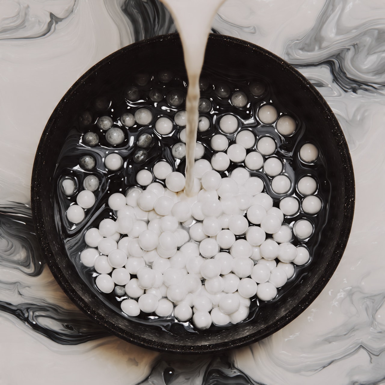 Inside a black cooking pot, there is one visible layer of white small solid pieces that look soft and round, with creamy white liquid being poured over them from above. The inside of the pot is smooth and dark, creating contrast with the white contents. The background is a white marbled texture. photo taken with an iphone --ar 4:5 --v 7