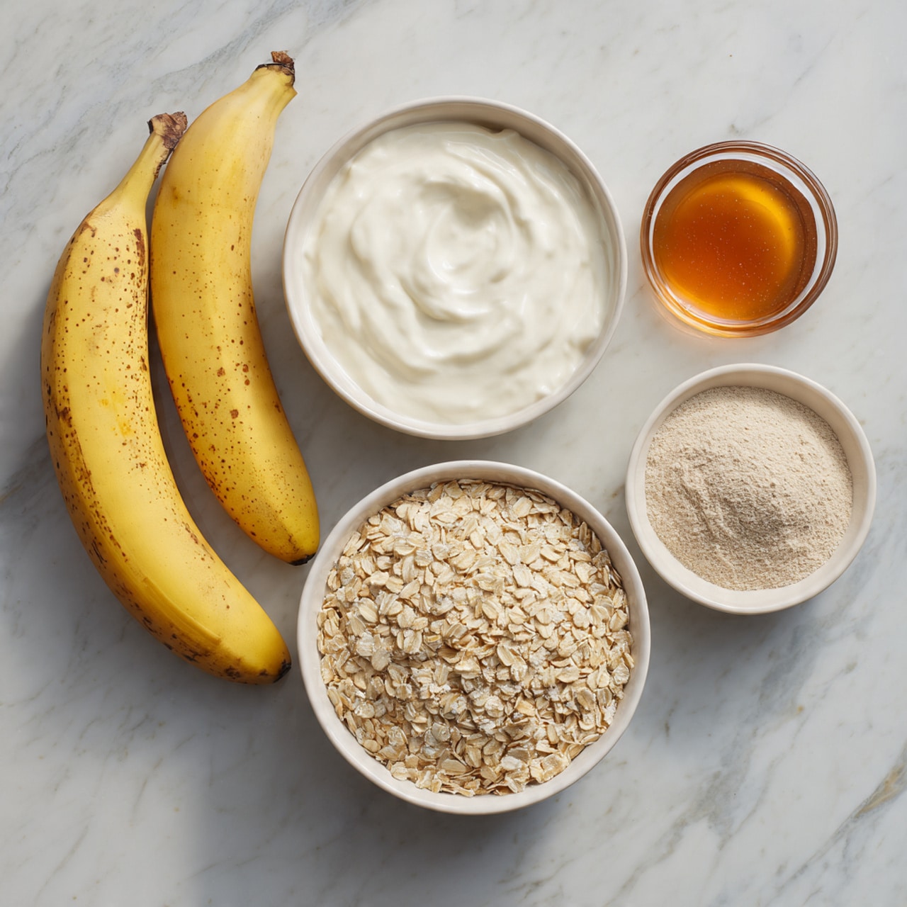 The image shows five main ingredients arranged neatly on a white marbled surface. Two yellow bananas with brown spots lie next to a white bowl filled with thick, creamy white Greek yogurt. Below them is a larger white bowl filled with a layer of pale rolled oats. To the left of the oats is a smaller white bowl containing a fine, light beige protein powder. To the right of the oats, there is a small glass container with a smooth, amber-colored maple syrup. All items are spread evenly and clearly visible for easy identification. Photo taken with an iphone --ar 4:5 --v 7