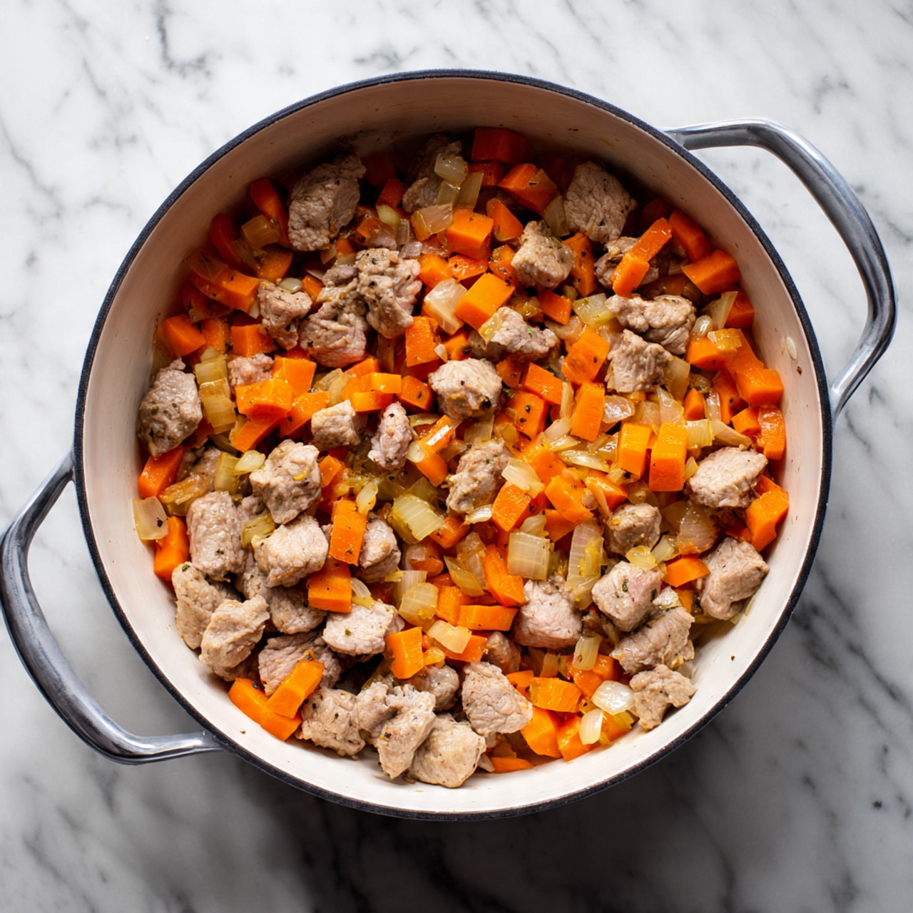 The image shows a white pot filled with cooked small pieces of brown meat mixed with chopped orange carrots and pale yellow onions. The ingredients are evenly spread inside the pot, with the meat chunks being the largest pieces and the carrots and onions smaller and more chopped. The colors contrast well, with the bright orange of the carrots standing out against the brown meat and light onions. The pot is placed on a surface with white marbled texture. The pot’s handles are silver and curved. Photo taken with an iphone --ar 4:5 --v 7