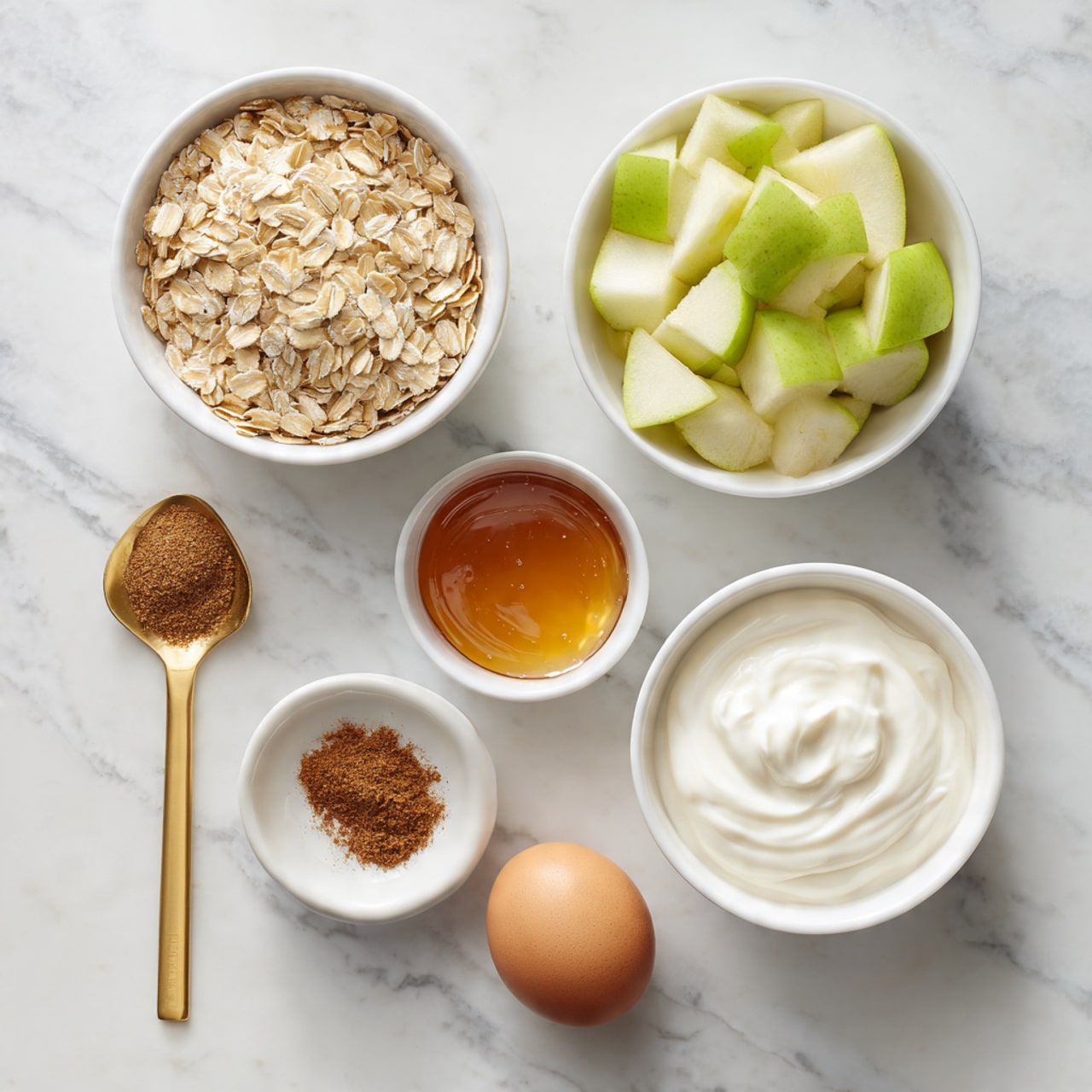 The image shows six ingredients arranged neatly on a white marbled surface. At the top left, a white bowl is filled with light tan rolled oats. To the right, there is a white bowl filled with chopped greenish-yellow apples. Below the oats, a white bowl holds smooth, creamy white Greek yogurt. Next to the yogurt on the right side, a small white bowl contains amber-colored maple syrup. Below the maple syrup, a single brown egg lies on the surface. To the left of the egg, a gold spoon holds a small amount of ground cinnamon, a dusty brown spice. The ingredients are spaced evenly in a loose circle. Photo taken with an iphone --ar 4:5 --v 7