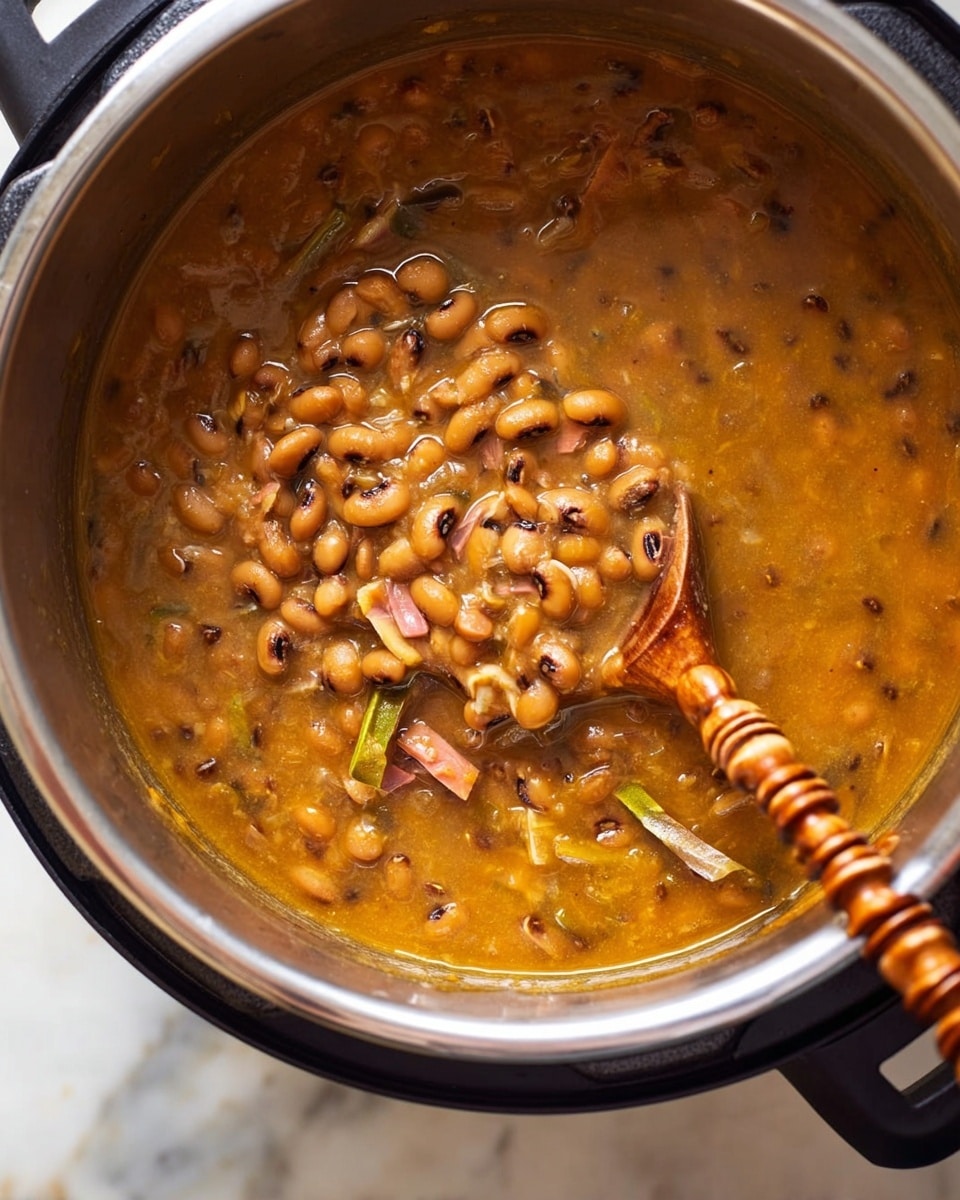 A close-up view of a thick stew inside a shiny metal pot with black handles on a white marbled surface. The stew is golden brown with black-eyed beans scattered throughout and small pieces of green and pink ingredients visible. A wooden spoon with a twisted handle is partially submerged in the stew, lifting some of the beans and liquid. The texture looks hearty and slightly chunky with a glossy finish. photo taken with an iphone --ar 4:5 --v 7