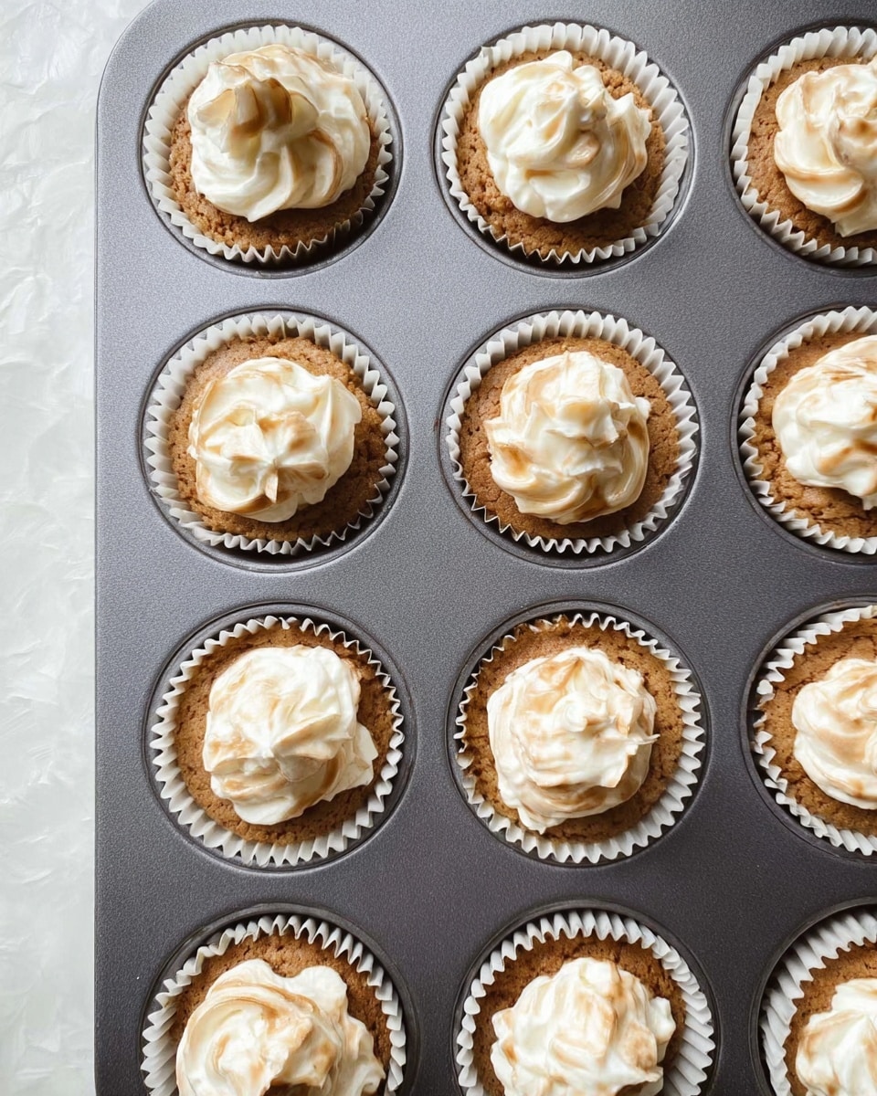 The image shows nine cupcakes in a grey muffin tray, each with two layers. The bottom layer is light brown with a slightly rough texture, and the top layer is creamy white, swirled softly into the brown base. Each cupcake is held in a white paper liner, and the surface underneath the tray has a white marbled texture. The lighting is even and natural. photo taken with an iphone --ar 4:5 --v 7