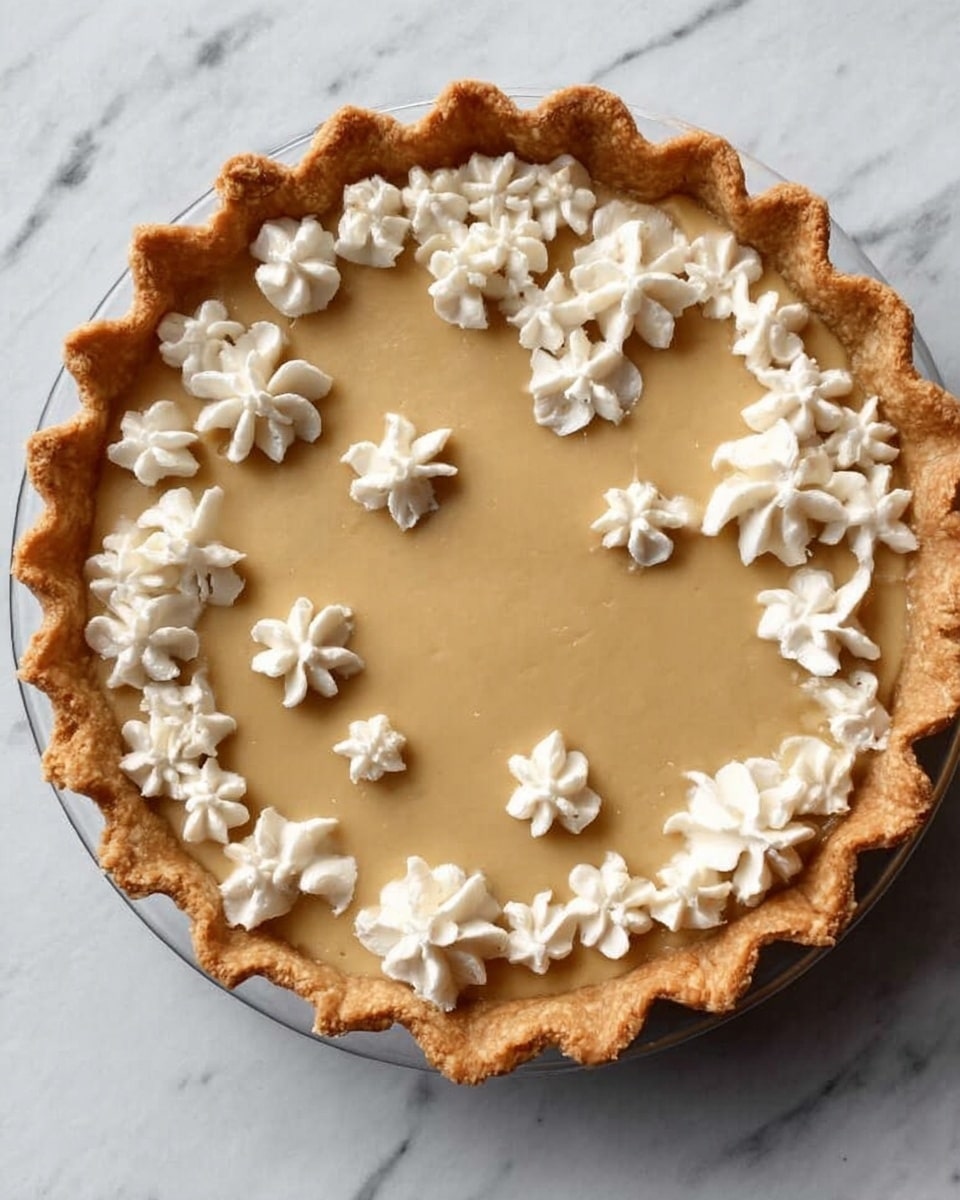 A slice of light golden pie sits on a white plate with a thick, evenly baked crust forming the base and edges. The filling is smooth and pale yellow, topped with a drizzle of glossy caramel sauce that also spreads around the plate. Three small swirls of fluffy white whipped cream sit near the wider edge of the slice, adding texture and contrast. The background is a soft white marbled texture, and another slice of the same pie blurred in the distance behind. Photo taken with an iphone --ar 4:5 --v 7