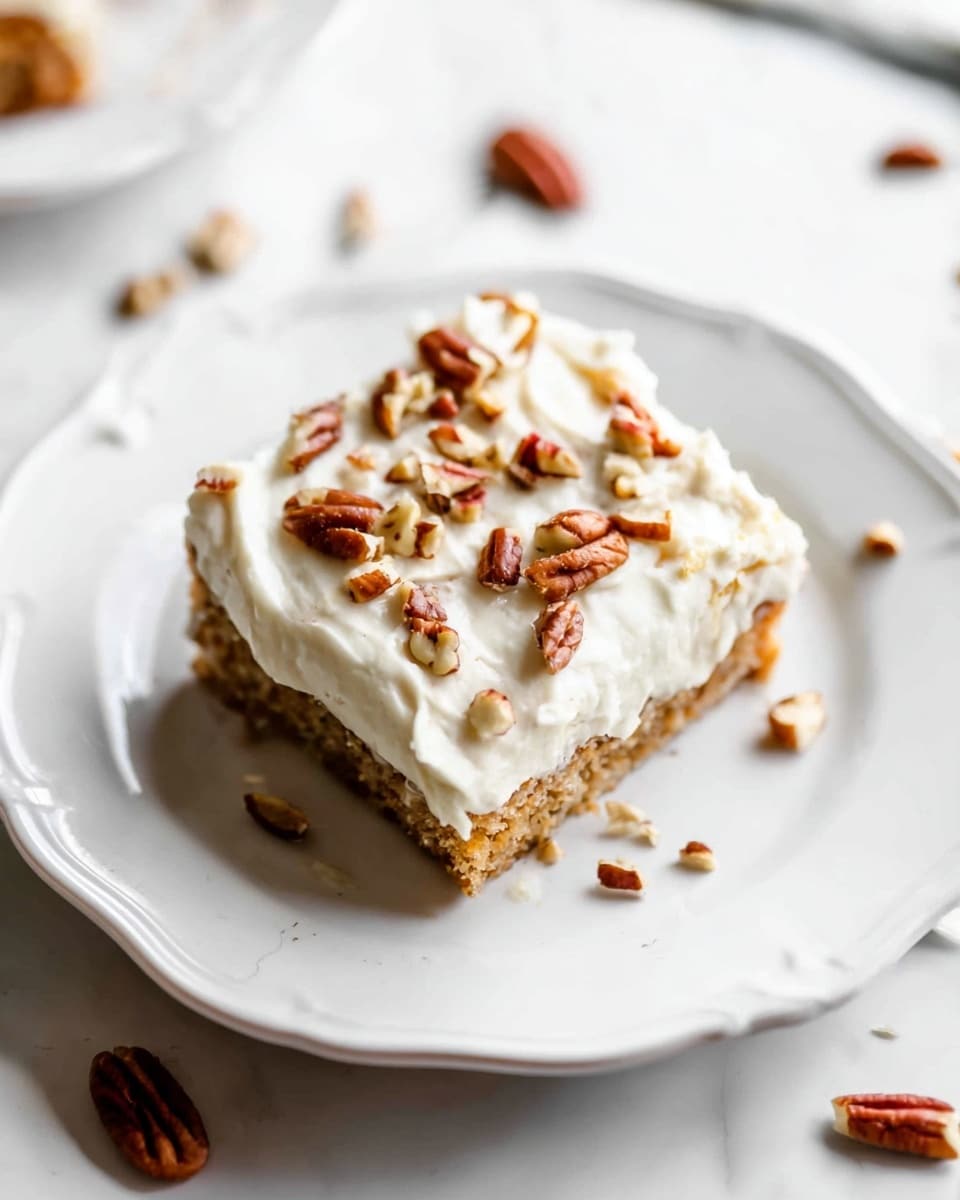 A single square piece of layered cake is placed in the center of a white plate with a scalloped edge. The cake has two visible layers: a light brown base and a thick creamy white frosting layer on top. The frosting looks smooth and fluffy, covering the entire top surface. Scattered over the frosting are unevenly chopped pecans in shades of brown, adding texture and contrast. The plate sits on a white marbled surface with a few pieces of pecans around it, all shown in bright natural light. photo taken with an iphone --ar 4:5 --v 7
