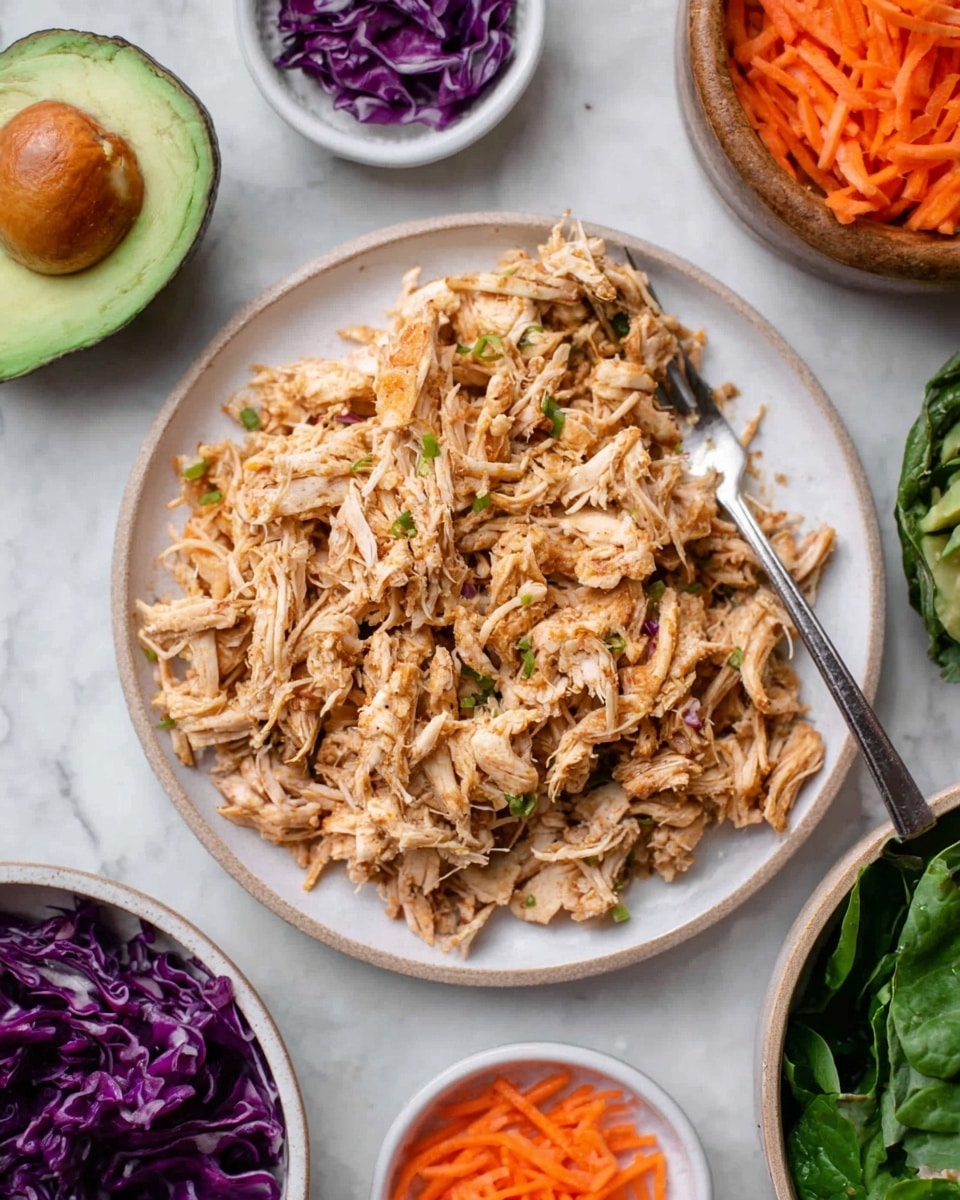 The image shows a white plate filled with shredded cooked chicken that has a light brown color with some small darker bits mixed in. A silver fork rests on the right side of the plate, partially in the chicken. Around the plate, various small white bowls hold thin orange carrot strips and purple cabbage shreds, while the upper part of the image shows half of an avocado with its seed removed. Dark green leafy vegetables are arranged at the bottom right corner. The dish and ingredients sit on a white marbled surface. Photo taken with an iphone --ar 4:5 --v 7