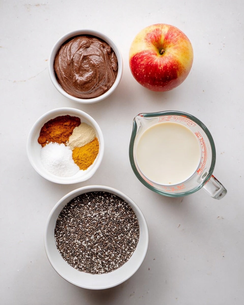 The image shows five separate ingredients arranged on a white marbled surface. There is a small white bowl filled with a smooth, dark brown paste on the top left, and below it, a smaller white bowl contains four powders in separate sections: white salt, light brown cinnamon, yellow turmeric, and beige ginger. In the center, a larger white bowl holds a dense pile of small black and white chia seeds. To the right, a clear glass measuring cup is filled with a creamy white liquid, and next to it, a fresh red and yellow apple rests on the surface. Photo taken with an iphone --ar 4:5 --v 7