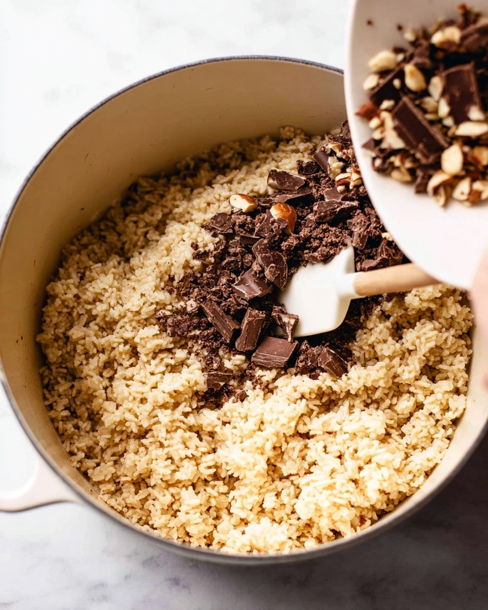A white pot filled with light golden crispy rice cereal mixed with small beige clusters. Dark brown chopped pieces of chocolate and nuts are being poured from a white bowl held by a woman's hand above the pot. Inside the pot, a white spatula stirs the mixture, showing a rough texture of the cereal and chocolate bits. The background is a white marbled surface. Photo taken with an iphone --ar 4:5 --v 7