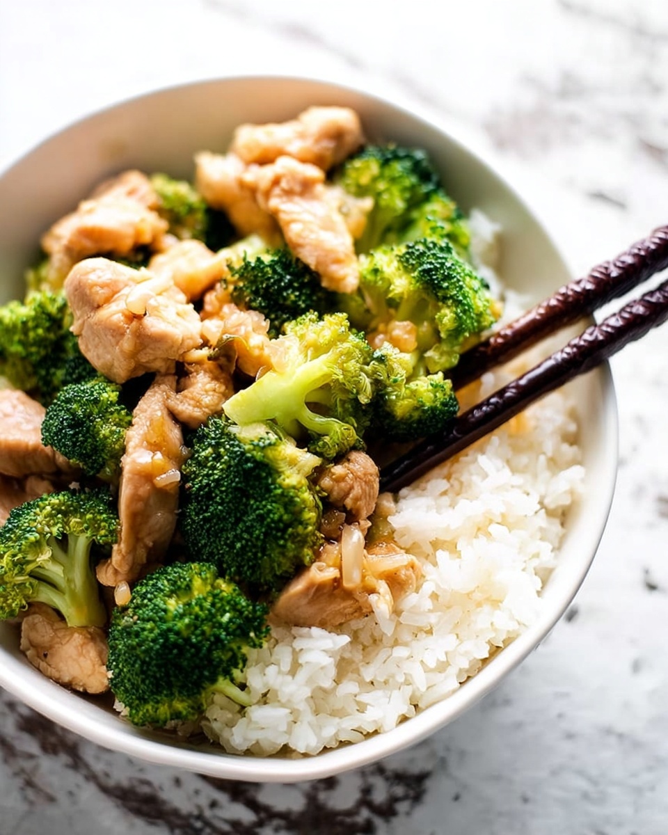 This image shows a round white bowl filled with three main layers. The bottom layer is steamed white rice, soft and fluffy. The middle layer has pieces of cooked chicken with a light brown color, showing a slightly shiny surface. The top layer has bright green broccoli florets, lightly cooked and placed all around the chicken pieces. A pair of dark brown chopsticks is resting in the bowl, picking up some broccoli and chicken. The bowl is placed on a white marbled surface. photo taken with an iphone --ar 4:5 --v 7