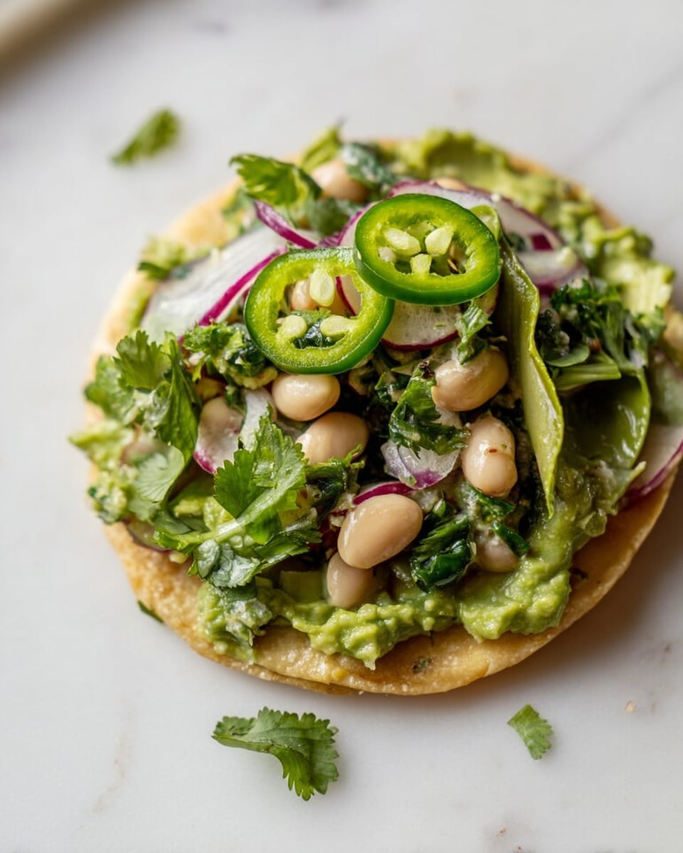 A single round crispy base with a light golden color sits on a white marbled surface, topped with a thick, chunky green spread likely made of mashed avocado or similar. On top of this are layers of white beans, thin slices of purple-red onion, bright green jalapeño rings with visible seeds, and fresh green cilantro leaves scattered around and on the dish. The textures vary from soft spread, the firm beans, and crisp peppers, creating a fresh and vibrant look. Photo taken with an iphone --ar 4:5 --v 7