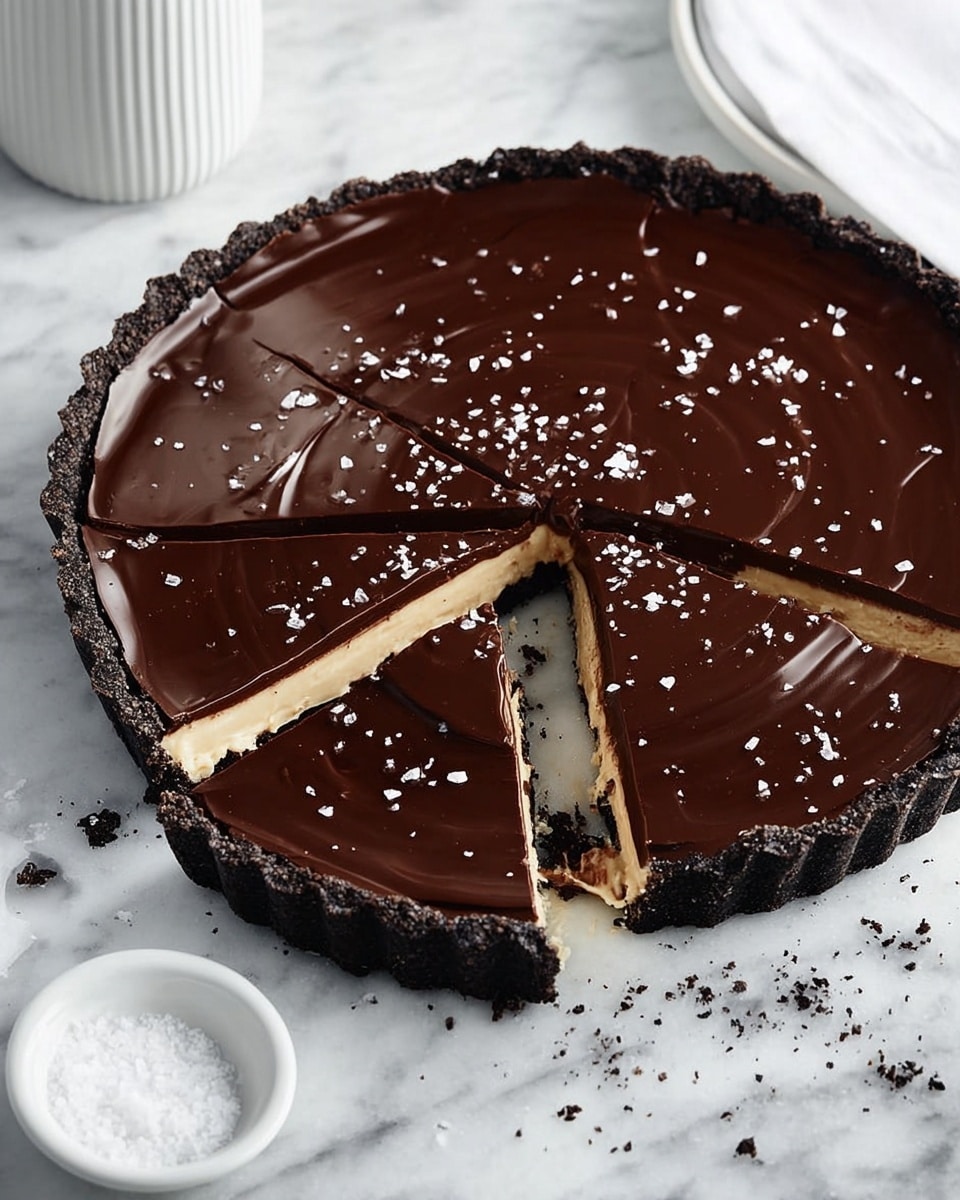 A round tart with three visible layers: the bottom crust is dark and crumbly, forming a thick edge; the middle layer is light tan and creamy; the top layer is a smooth, shiny dark chocolate glaze with some gentle ripples and small flakes of salt scattered over it. Several slices have been cut and slightly pulled apart near the center, revealing all layers clearly. The tart is placed on a white marbled surface with some crumbs around it, and a white container and a small white dish with salt sit in the background. Photo taken with an iphone --ar 4:5 --v 7