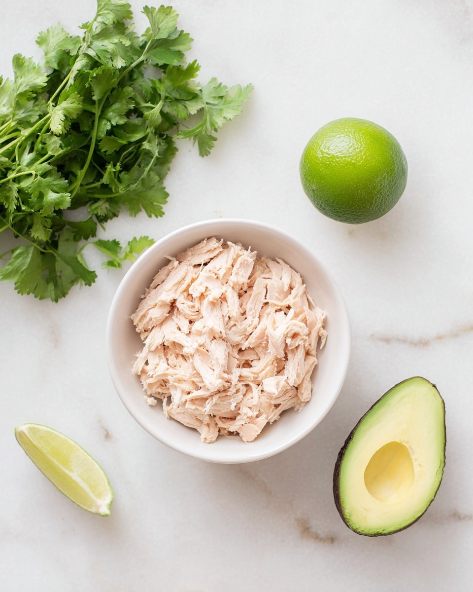 A white bowl filled with light pink shredded chicken sits on a white marbled surface, next to a bunch of fresh green cilantro leaves on the upper left side, a whole bright green lime on the middle right, and a dark green avocado half with a yellow-green inside on the lower right. The ingredients are evenly spaced, showing a fresh and simple arrangement. photo taken with an iphone --ar 4:5 --v 7