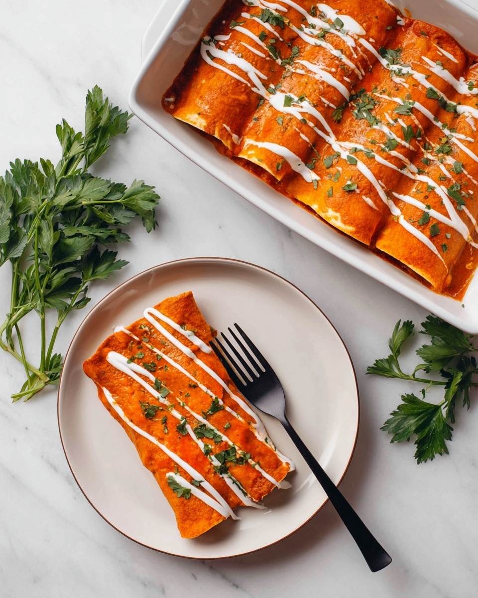Two rolled enchiladas covered with a smooth orange-red sauce topped with white cream drizzles and small green herb bits sit on a round white plate. A black fork rests beside the enchiladas on the plate. In the top left is a white rectangular baking dish filled with several similar enchiladas, also covered with the same orange-red sauce and white cream drizzles. Fresh green parsley sprigs lie on a white marbled surface around the plate and dish. photo taken with an iphone --ar 4:5 --v 7