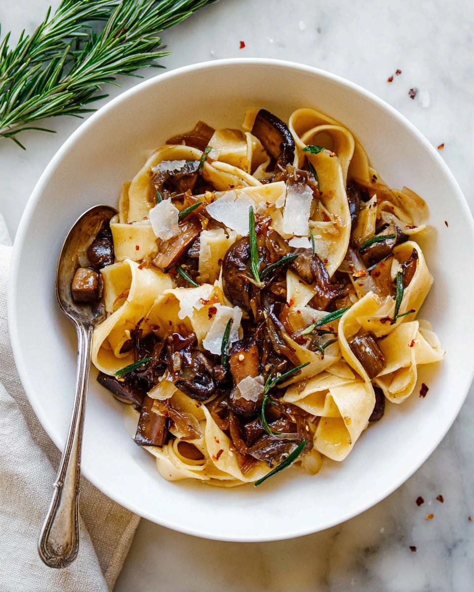 A white bowl filled with wide, flat noodles that are light yellow in color and slightly curled at the edges. Mixed among the noodles are chunky pieces of dark brown mushrooms and small bits of caramelized onions with a glossy texture from sauce coating them. There are thin green rosemary sprigs scattered on top, along with small, thin white shavings of cheese and a few red pepper flakes sprinkled throughout. On the left edge of the bowl, there is a vintage silver spoon resting. The bowl sits on a white marbled textured surface with a small bunch of fresh green rosemary in the top left corner. Photo taken with an iphone --ar 4:5 --v 7