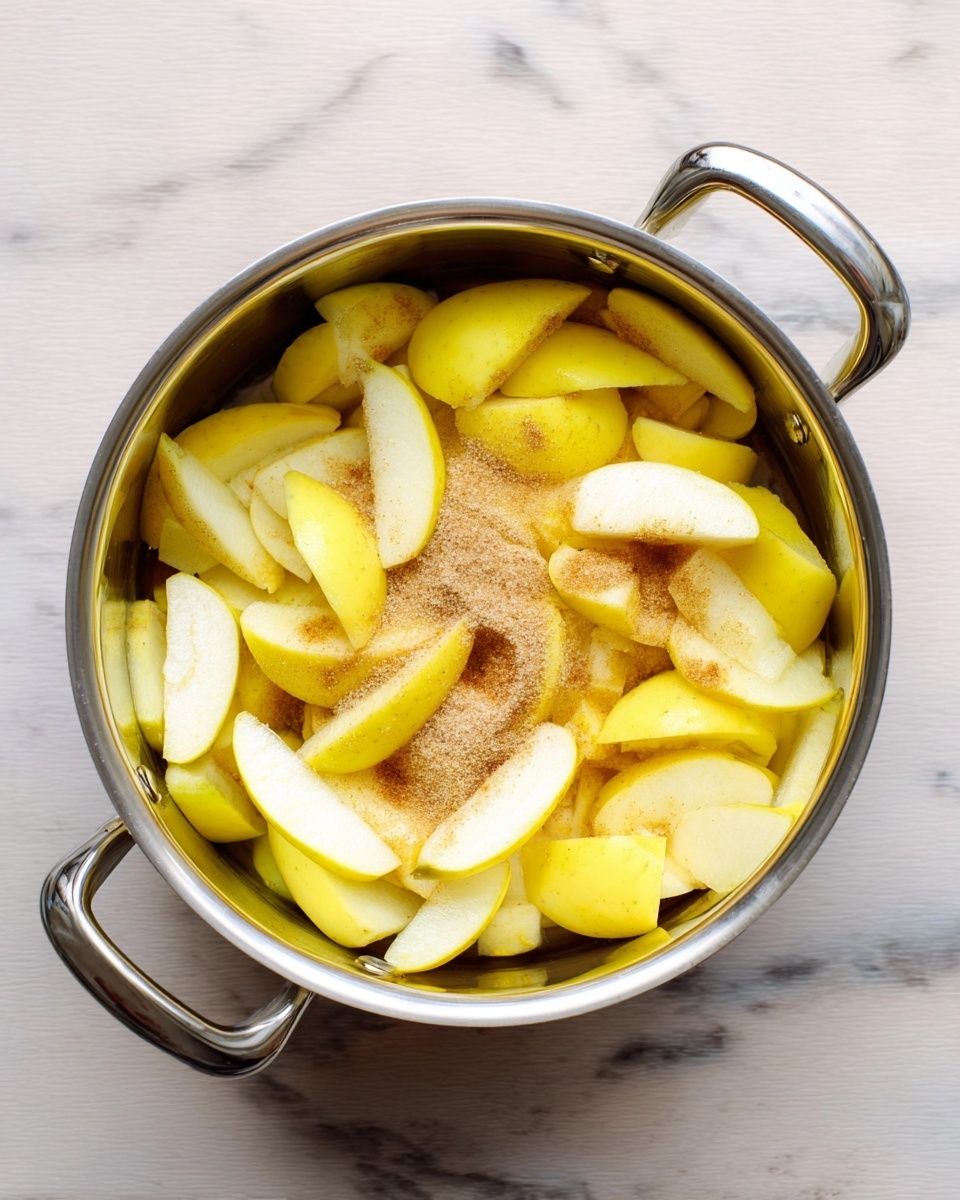 A silver cooking pot filled with many peeled and sliced yellow apples, mixed with white sugar and a light brown powder, placed on a white marbled surface. The apples are arranged mostly in layers, with whole peels resting on top and the sugar and powder scattered around them. The texture of the apples looks smooth and shiny, and the pot handles are visible on both sides. photo taken with an iphone --ar 4:5 --v 7