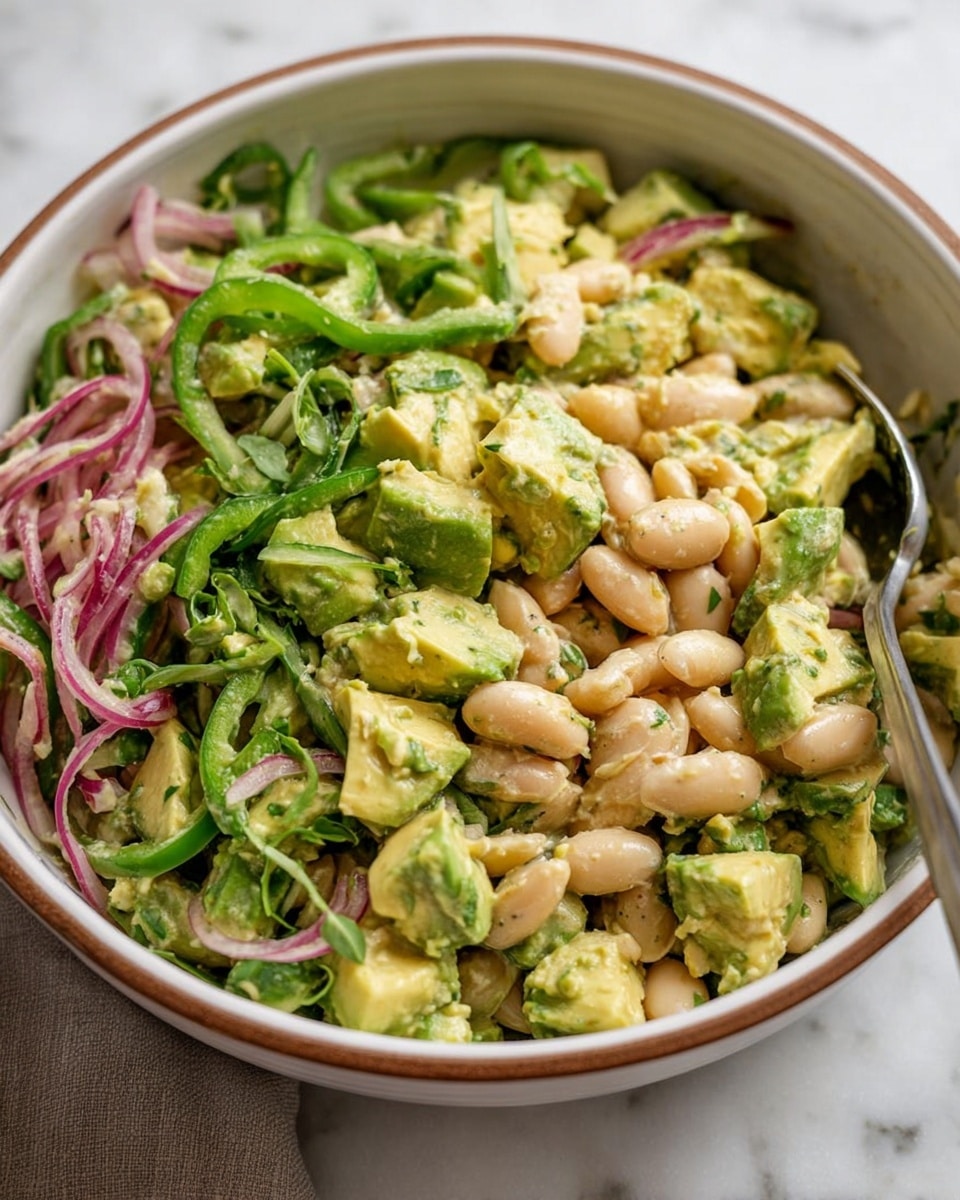 A close-up of a bowl filled with a fresh salad showing three main layers: at the bottom, a mix of light green chopped avocado and pale yellow chunks of cooked vegetable; the middle layer has creamy white beans scattered evenly; the top layer includes thin slices of green bell pepper, thin curved strips of red onion, and small green herb sprigs. The salad looks creamy with a light dressing that coats the ingredients. The bowl is white with a brown rim, placed on a white marbled surface. A metal spoon is partially visible inside the bowl. Photo taken with an iphone --ar 4:5 --v 7