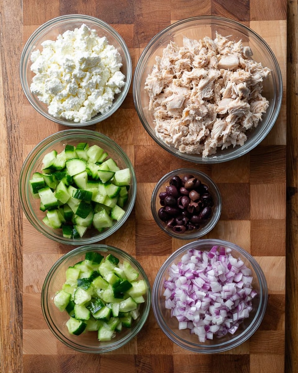 Five clear glass bowls sit on a wooden cutting board with a checkered pattern. The largest bowl, at the top right, holds shredded light-colored cooked chicken. To its left is a bowl filled with white crumbly cheese. Below the cheese, there is a bowl with chopped fresh cucumber, showing bright green skin and lighter green inside. To the right of the cucumbers is a bowl with finely chopped purple-red onions. At the bottom center, there is a small bowl with dark chopped olives. The photo taken with an iphone --ar 4:5 --v 7