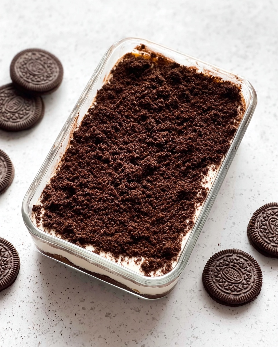 A close-up shows a spoon holding a scoop of layered dessert with a dark crumbly top layer, a creamy light brown middle layer, and some lighter cream beneath. The dessert is in a clear rectangular glass container on a white marbled surface. There are chocolate sandwich cookies around the container, and a woman's hand is holding the container as the spoon lifts out the dessert. The spoon is gold-colored, and the crumbly top looks like crushed chocolate cookies covering the creamy layers inside. photo taken with an iphone --ar 4:5 --v 7