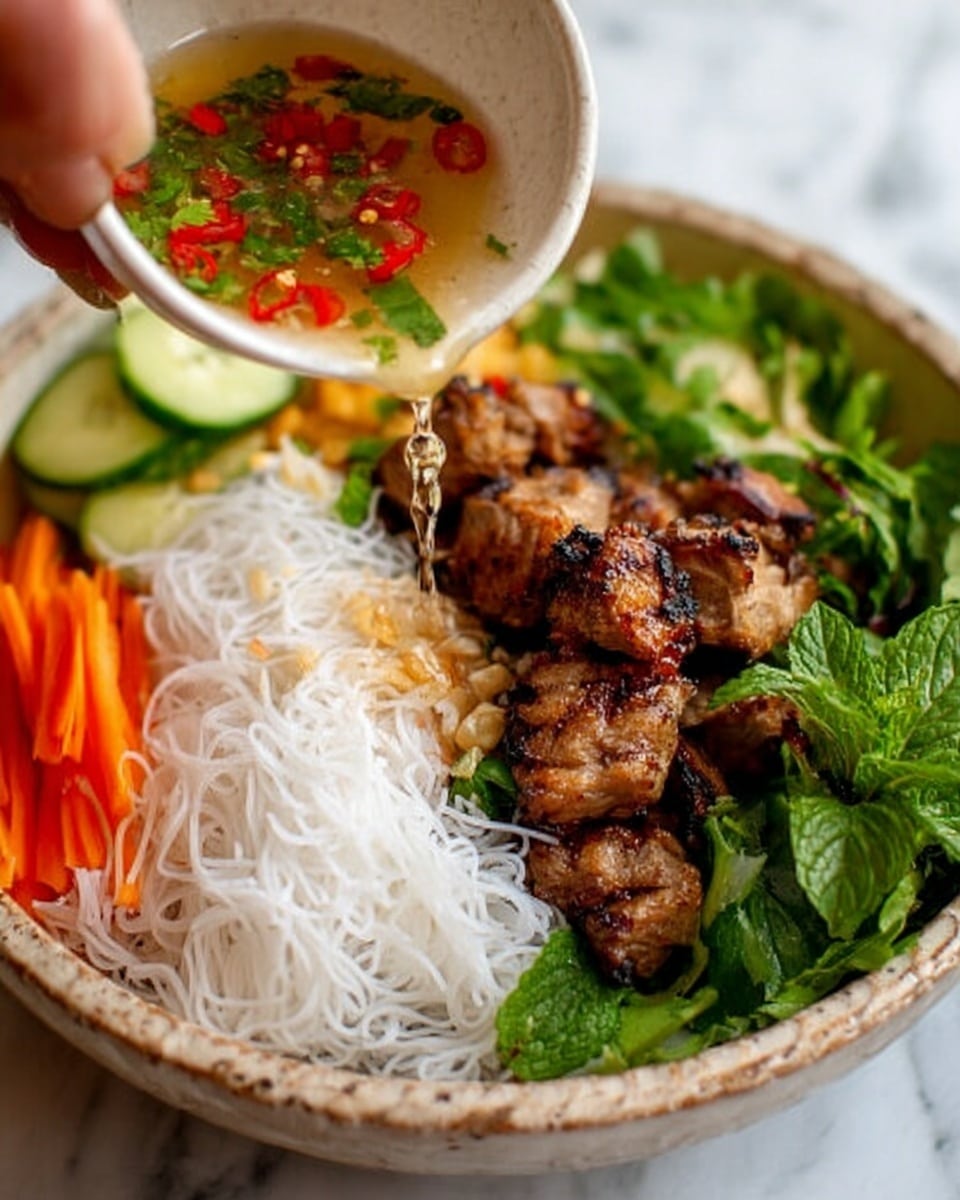 A close-up view of a bowl with white rice noodles forming a delicate nest on one side, golden-brown grilled meat chunks placed on the other side, and bright green fresh leafy herbs arranged around the edges. Sliced orange carrot sticks and pale green cucumber strips lie neatly in the background. A woman's hand holds a white bowl at the top left, pouring a clear sauce with floating red chili pieces and green herbs over the dish. The bowl sits on a white marbled surface. photo taken with an iphone --ar 4:5 --v 7