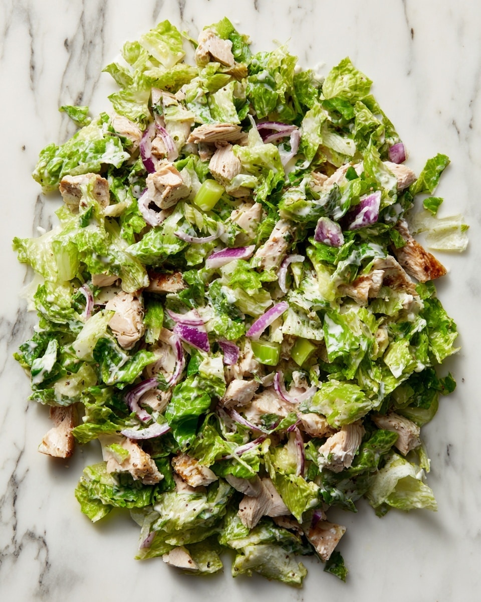 A mixed salad spread directly on a white marbled surface, showing roughly chopped green lettuce as the main layer, with pieces of cooked brown chicken scattered evenly throughout. Thin slices of purple onion and light green celery bits are mixed in, adding subtle color contrast. The salad is coated with a creamy dressing, visible as a light glossy texture over all ingredients, giving a fresh and appetizing look. No plate is shown, just the salad on the marble, and the overall image has a casual, natural style. photo taken with an iphone --ar 4:5 --v 7