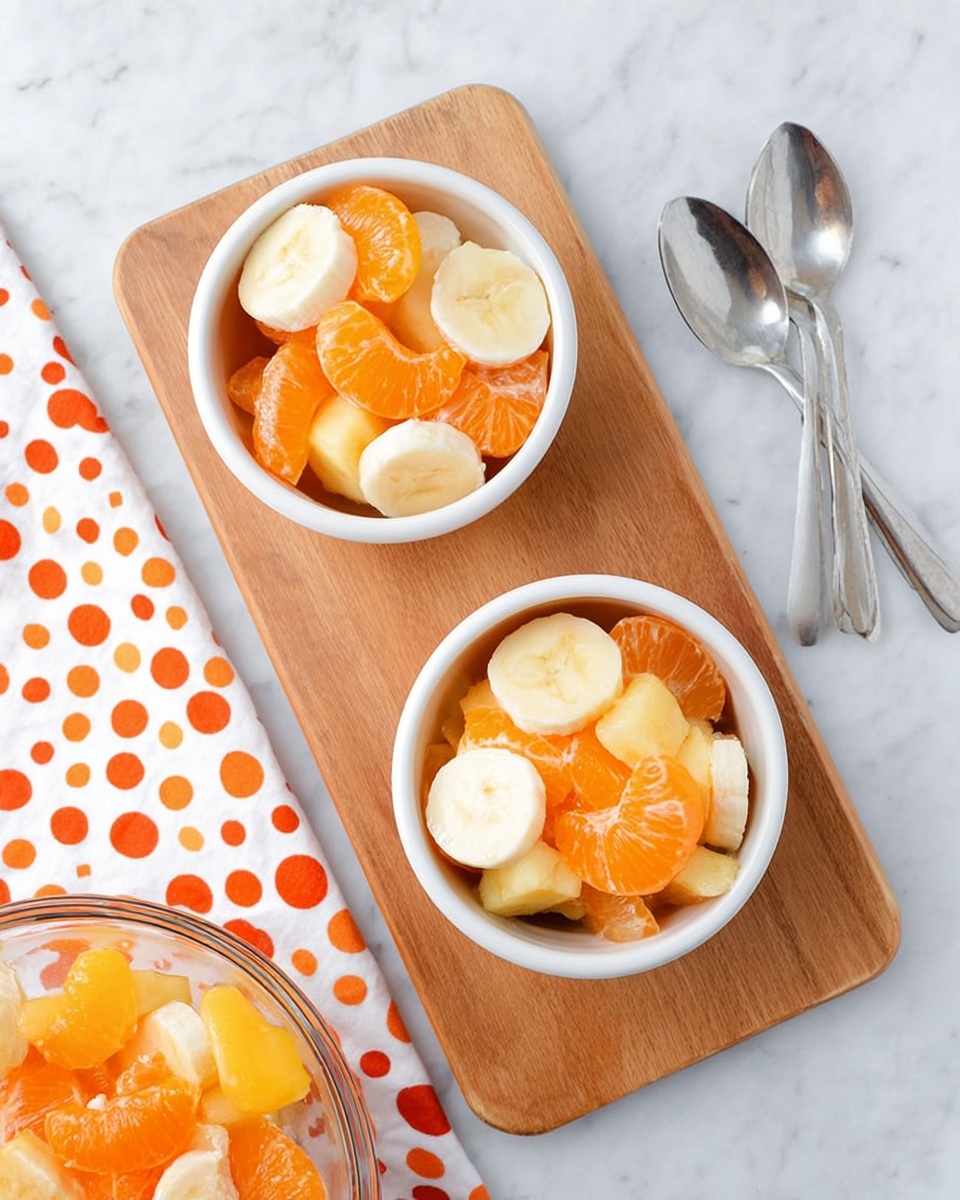 Two small white bowls sit on a light wooden board, each filled with a colorful fruit salad made of orange mandarin segments, round pale banana slices, and white pineapple chunks. The fruit pieces create a mix of bright orange, creamy yellow, and soft white colors layered randomly. Below the board, a clear glass bowl shows more fruit salad with the same fruits. To the top right, two shiny silver spoons rest on a white cloth with large bright orange polka dots. Everything is placed on a white marbled surface. photo taken with an iphone --ar 4:5 --v 7