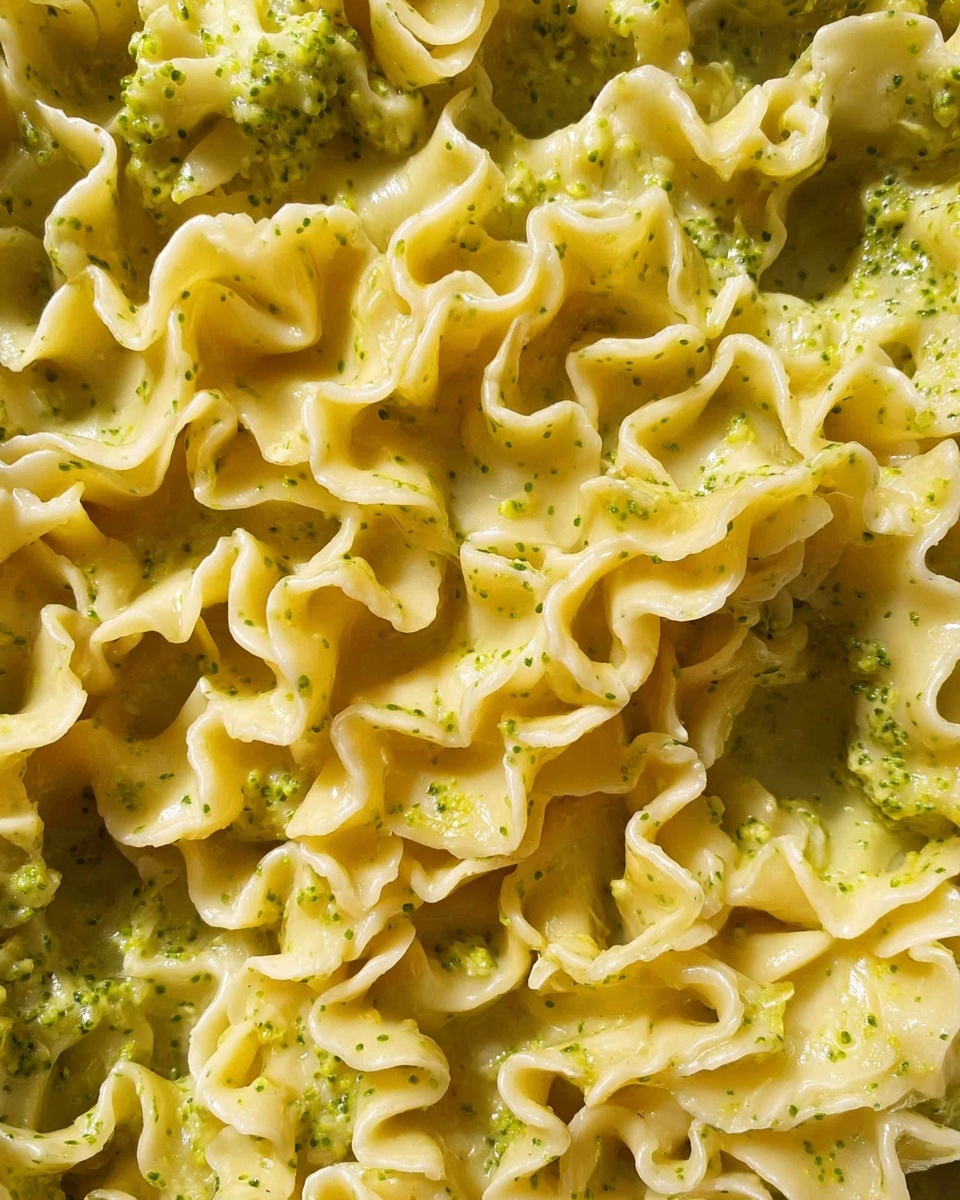 A close-up view of a pan filled with pasta that has wavy edges, covered in a creamy light yellow sauce with green herb bits mixed throughout. A woman's hand is holding a spoon lifting a portion of the pasta from the pan, showing the thick texture of the sauce clinging to the noodles. The pan is sitting on a white marbled surface, and the light highlights the smooth creaminess of the sauce along with the fresh green herbs. photo taken with an iphone --ar 4:5 --v 7